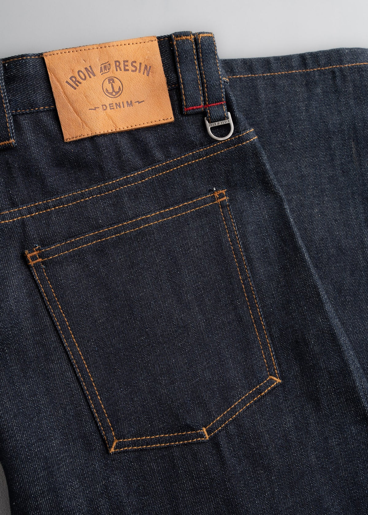 Dark denim jeans with a leather "Iron and Resin" patch, visible back pocket, and belt loop detail.