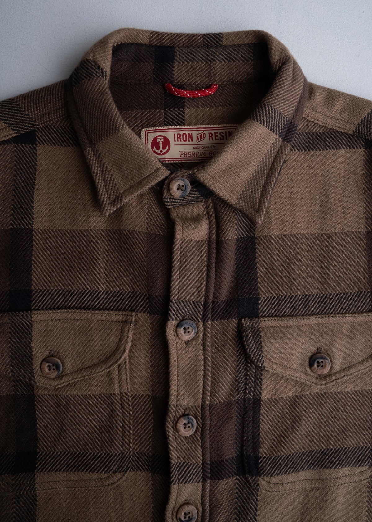 Brown plaid shirt with buttoned pockets and a collar, featuring an Iron and Resin label, displayed against a light background.