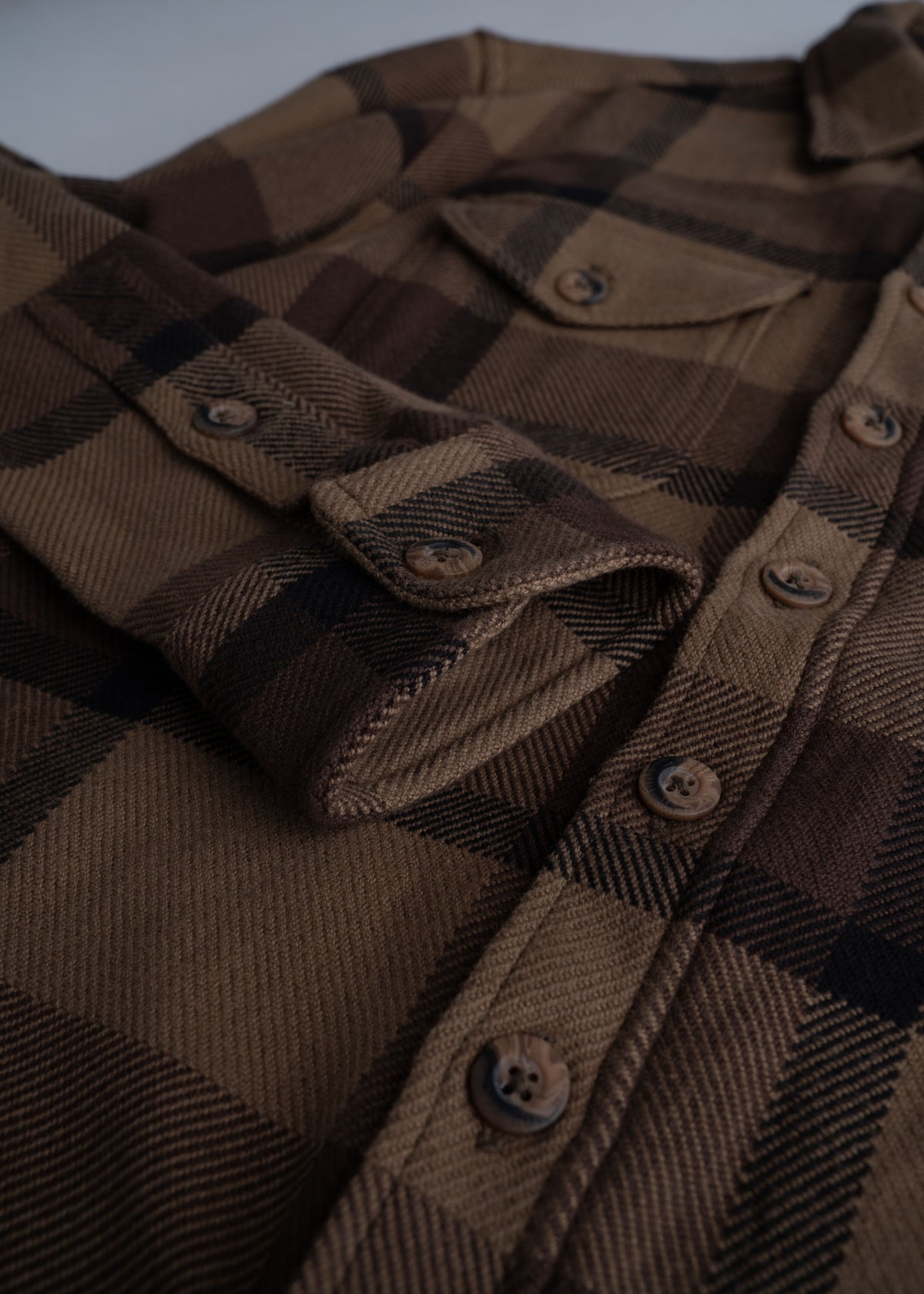 Close-up of a brown plaid shirt with button details and flap pockets, showcasing its textured fabric and classic design.