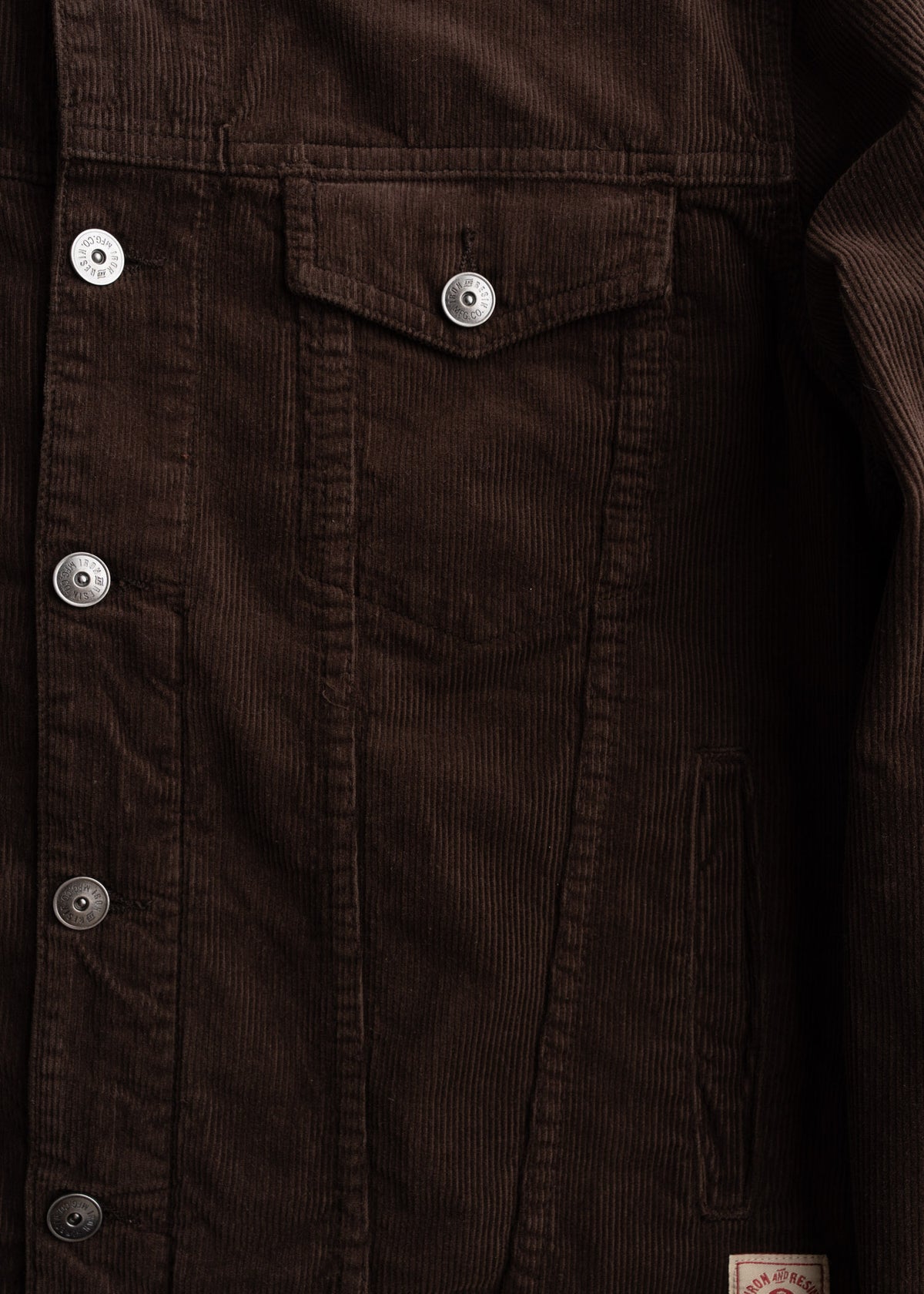 Brown corduroy jacket with silver buttons and a chest pocket, showcasing textured fabric and detailed stitching.