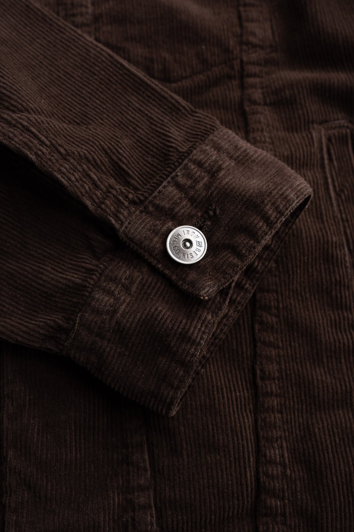 Close-up of a brown corduroy jacket sleeve with a silver button, showcasing texture and detail in the fabric and stitching.