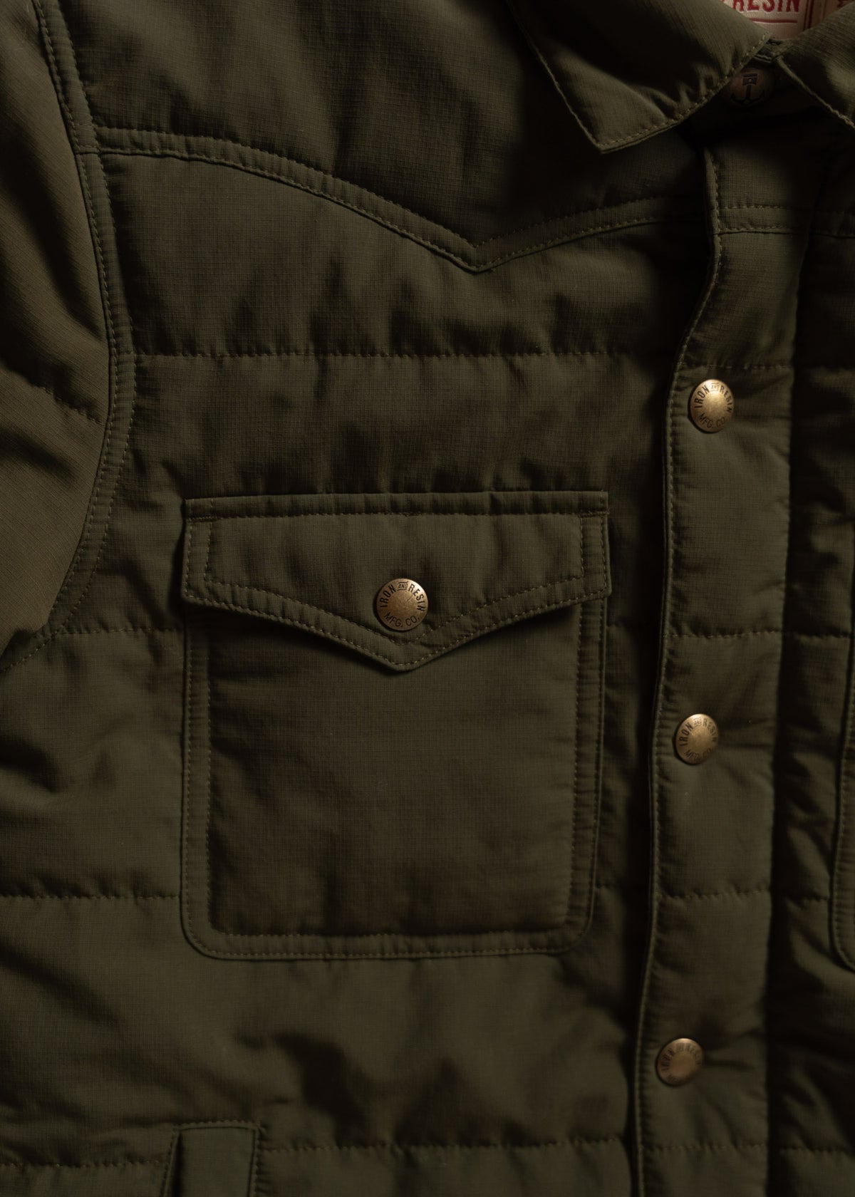 Close-up of an olive green quilted jacket with a front pocket and metallic snap buttons, highlighting its rugged texture.