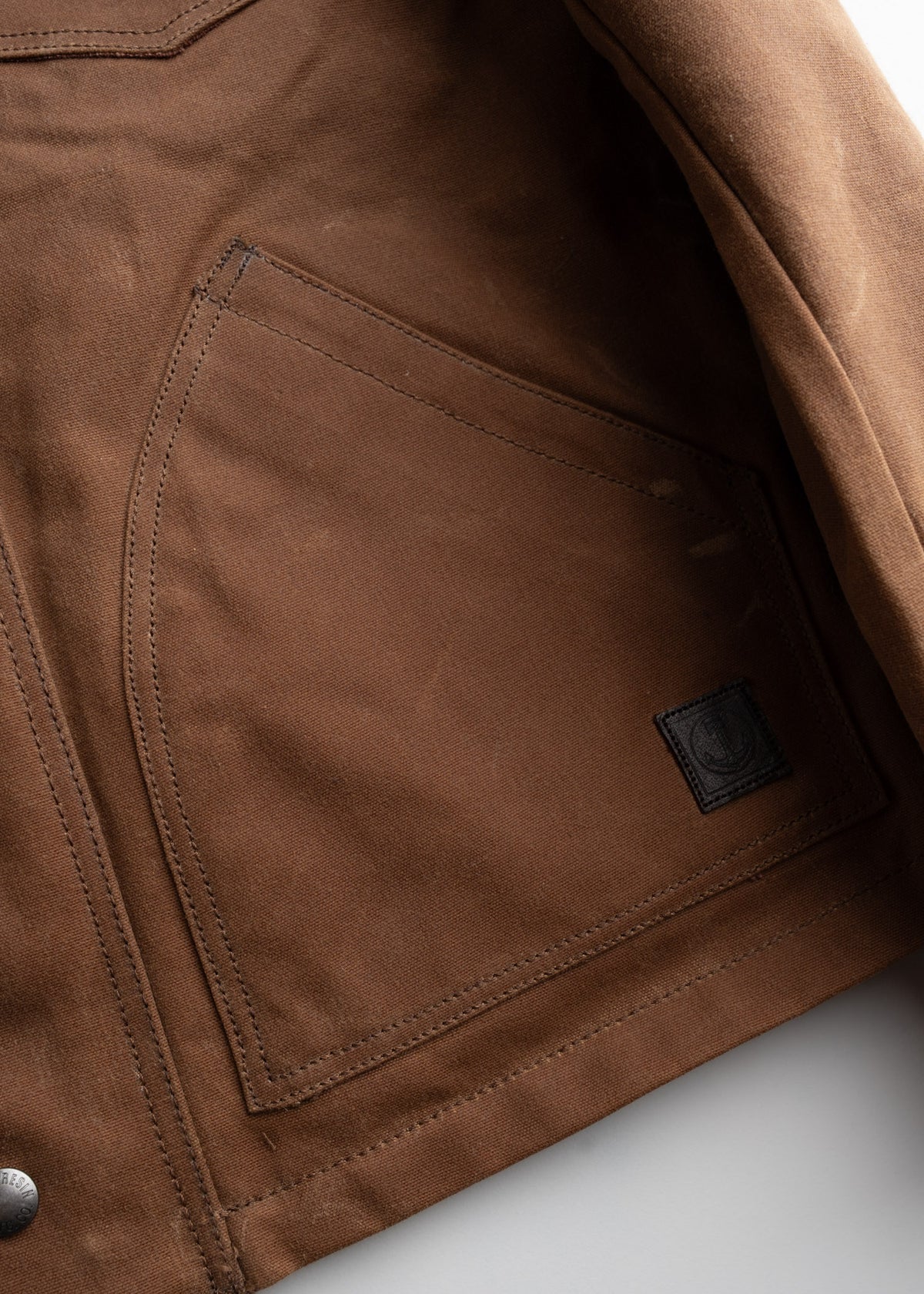 Close-up of a brown jacket pocket with visible stitching and a small black label on the side, highlighting its craftsmanship.