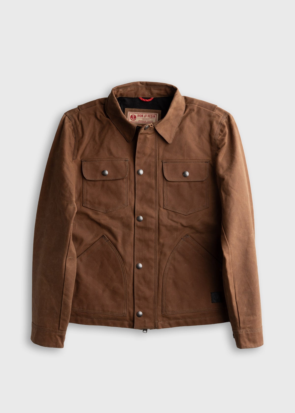 Brown waxed canvas jacket with metal buttons, two chest pockets, and a collar, displayed on a plain white background.