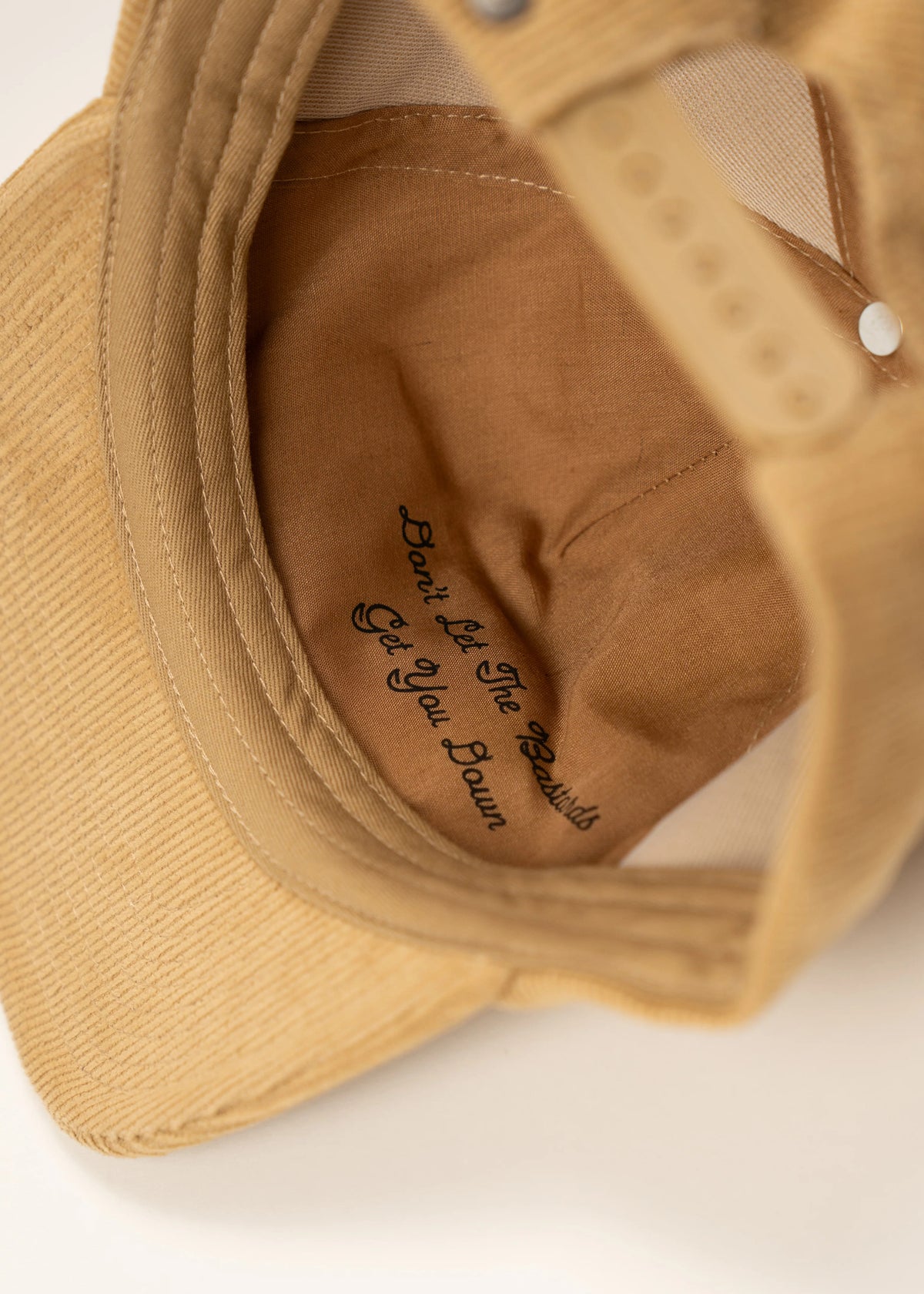 Inside view of a tan cap with the phrase "Don't let the bastards get you down" printed on the fabric.