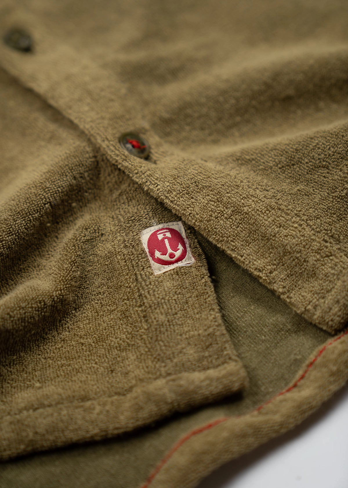 Close-up of a green textured fabric with a red logo tag and visible stitching, highlighting its detailed craftsmanship.