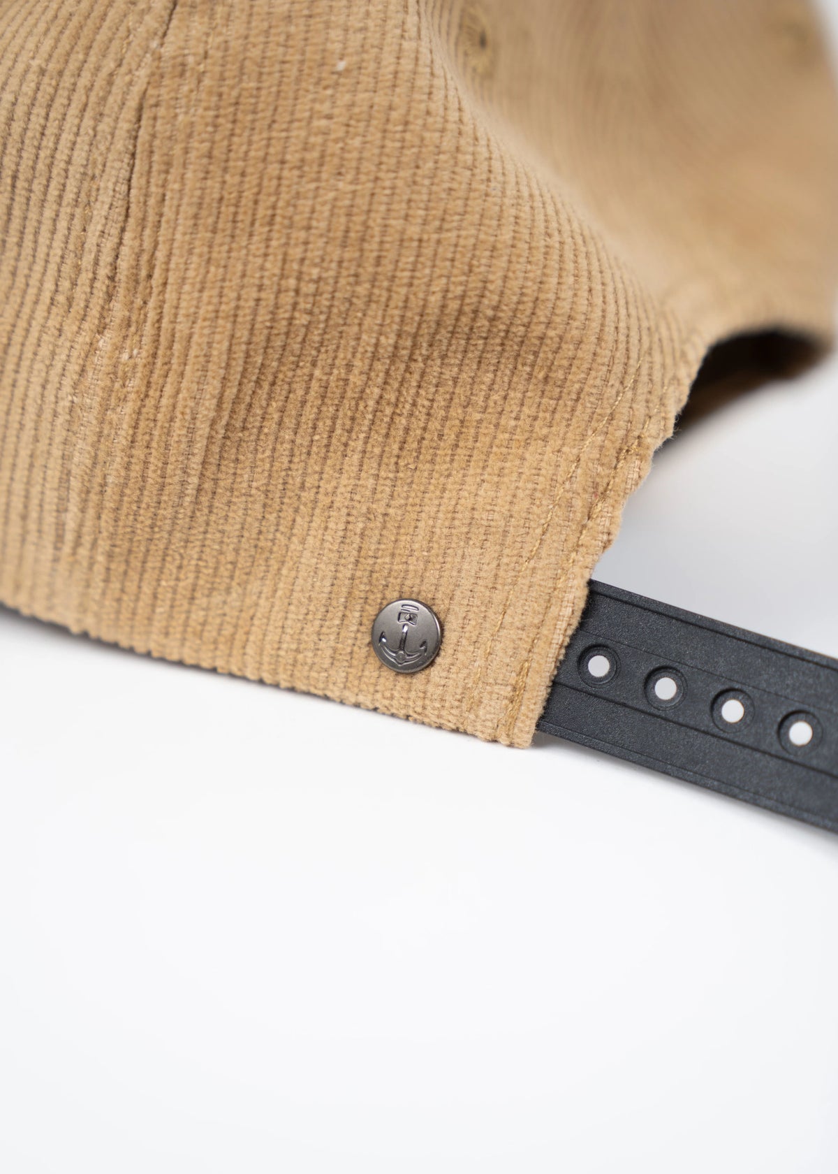 Close-up of a tan corduroy cap with a black adjustable strap and metal anchor button on a white background.