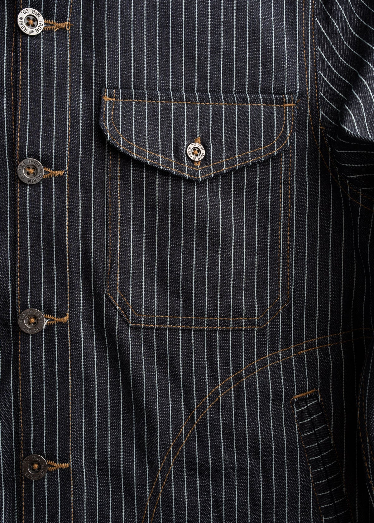 Close-up of a pinstripe denim jacket with brown stitching, featuring a buttoned pocket and visible buttons on the front.
