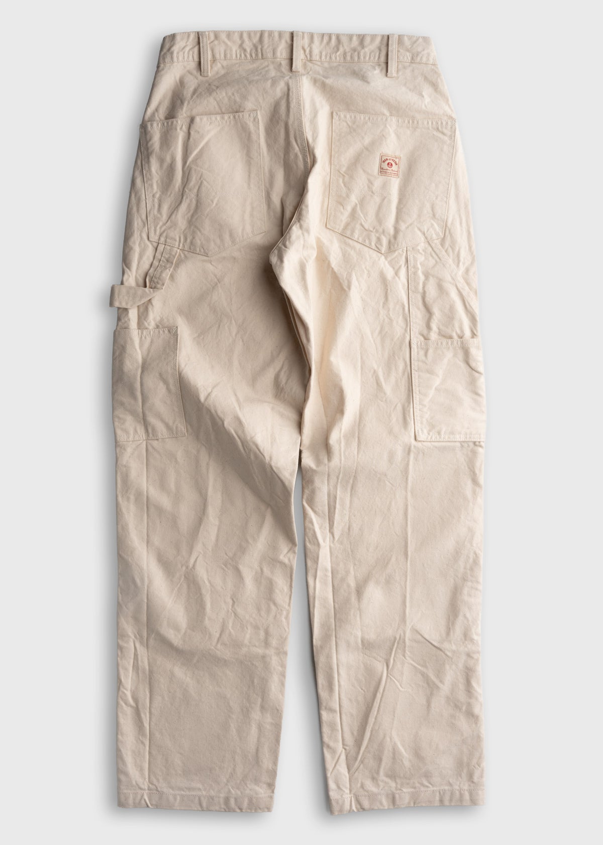 Beige work pants with multiple pockets and a small logo patch on the back, displayed against a plain white background.