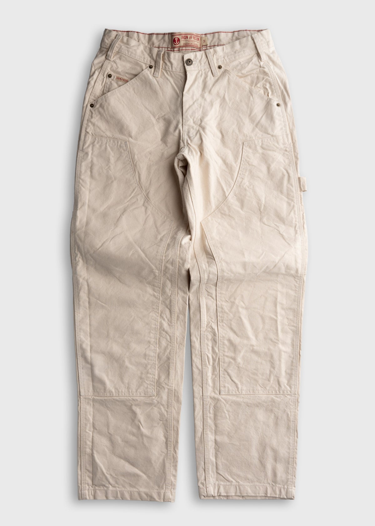 Cream-colored work pants with reinforced stitching and multiple pockets, laid flat on a white background.