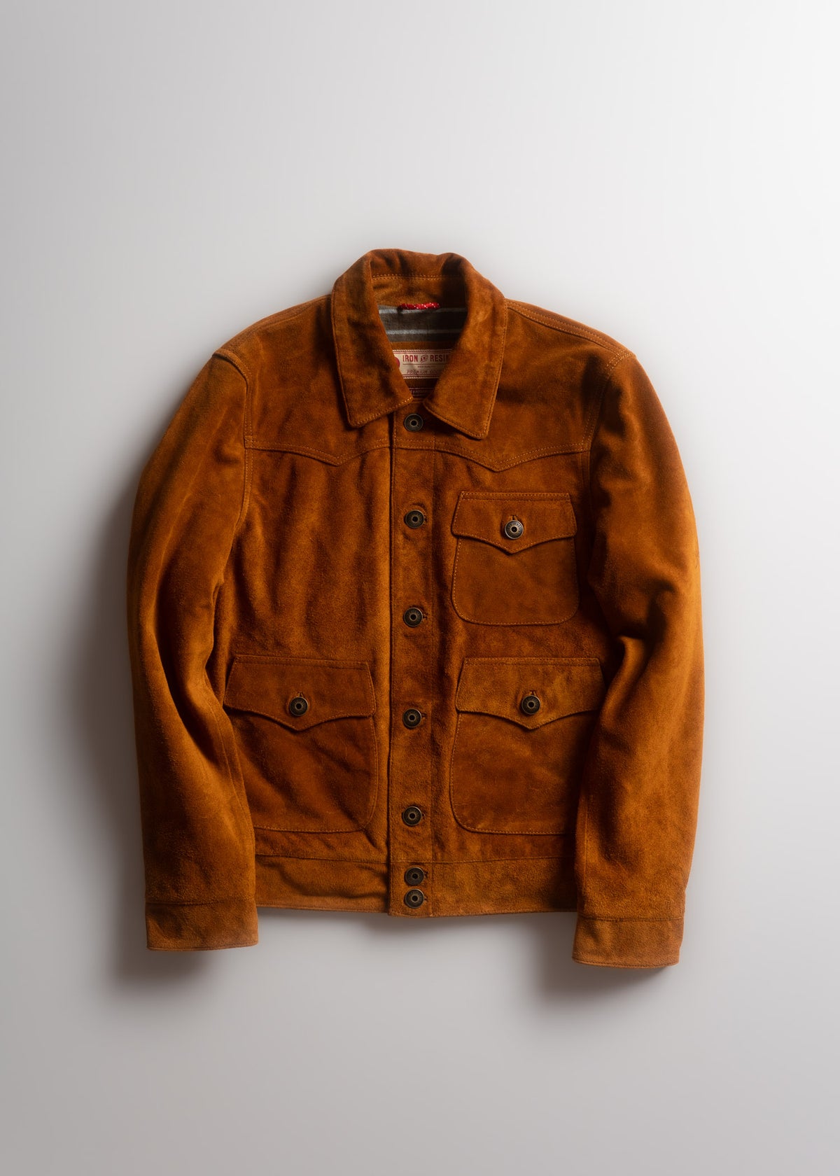 Brown suede jacket with button closure and four pockets, displayed on a white background, highlighting its classic design.