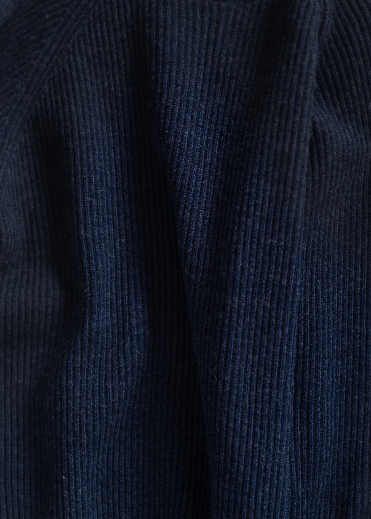 Close-up of dark blue ribbed fabric with soft folds, highlighting texture and depth in natural light.