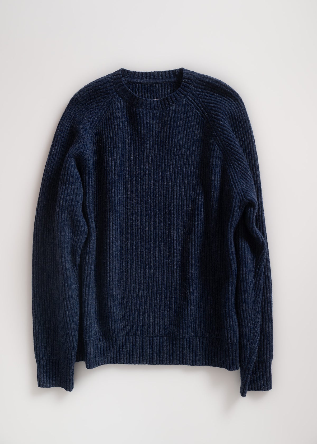A navy blue ribbed sweater is laid flat on a light background, showcasing its texture and classic crew neck design.