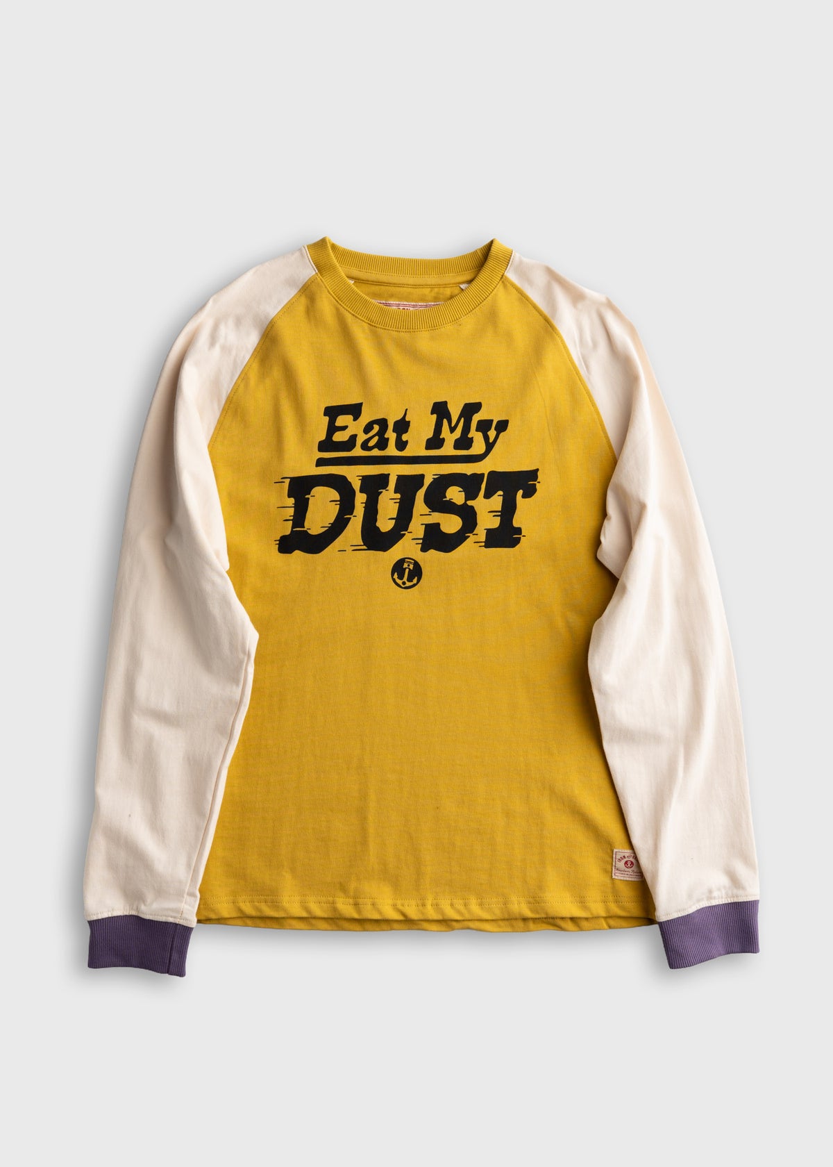 Yellow long-sleeve shirt with white sleeves, featuring bold text "Eat My Dust" in black. Purple cuffs add contrast.