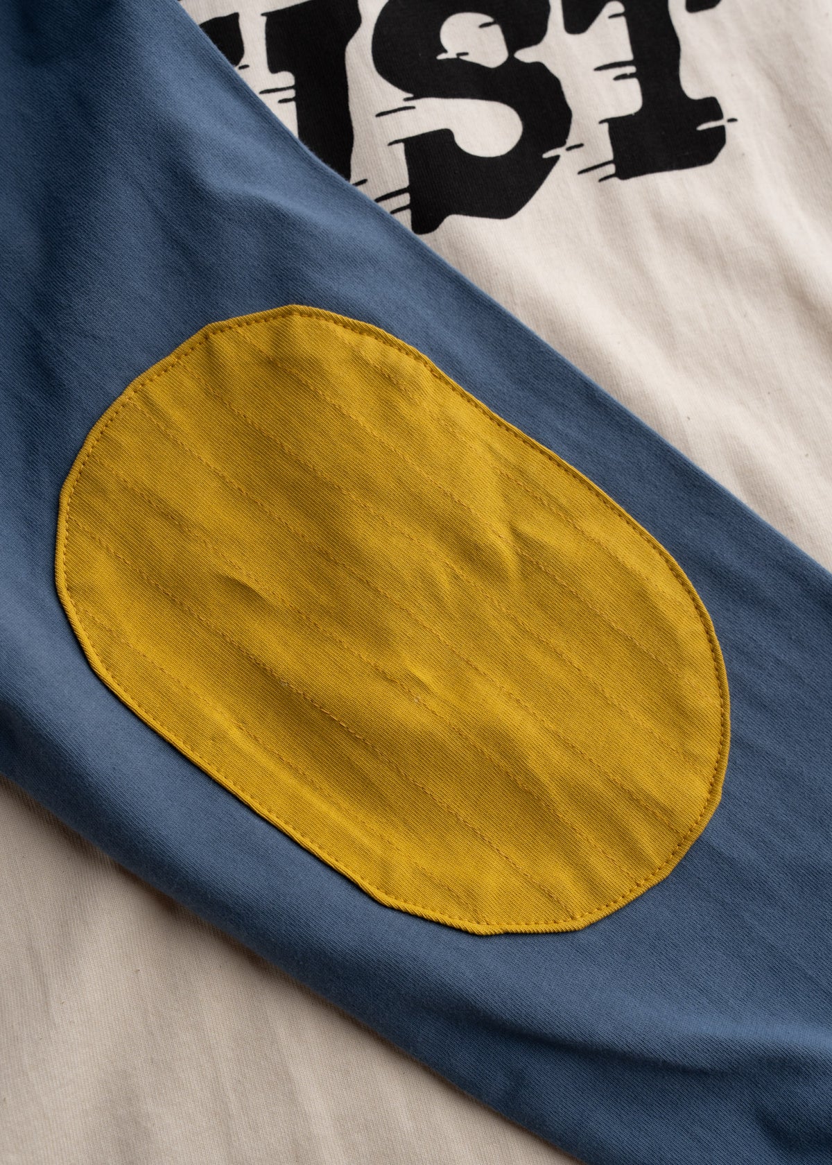 Close-up of a blue sleeve with a yellow elbow patch, next to white fabric with bold black text.