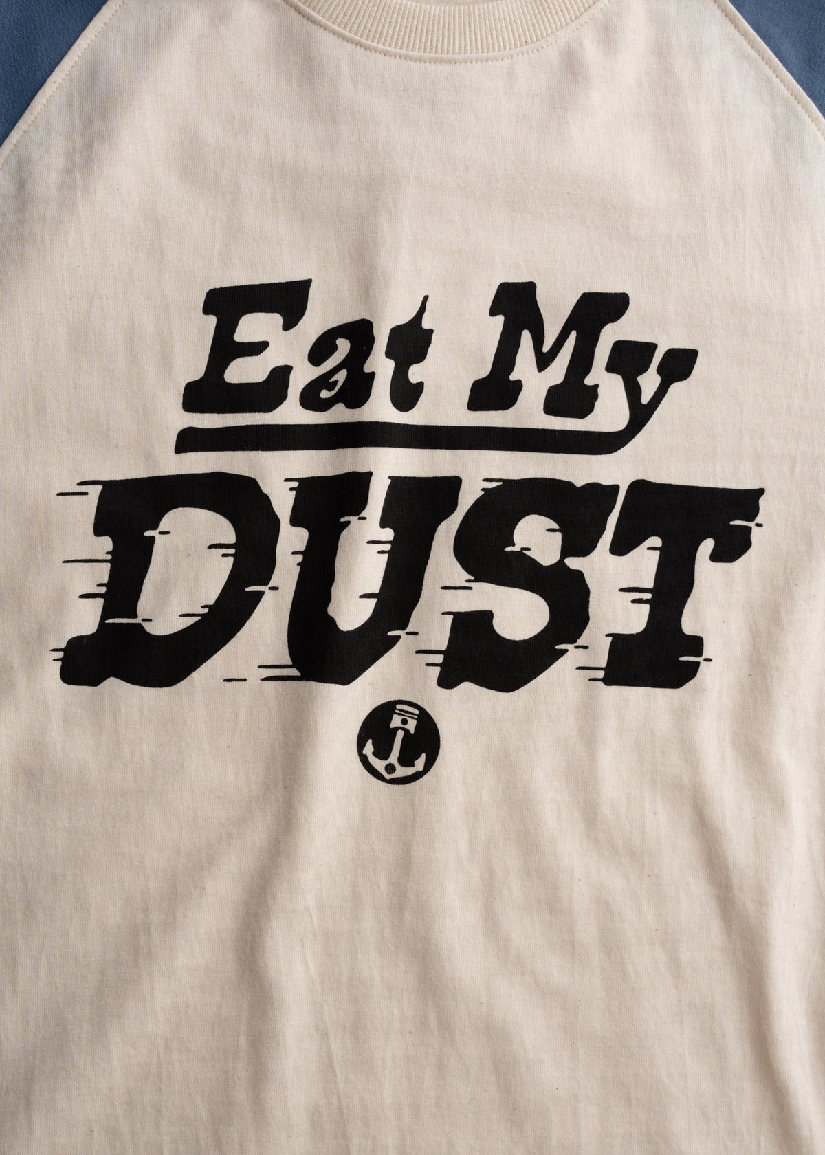 Beige shirt with bold black text "Eat My Dust" and a small anchor symbol below, creating a casual, playful statement.