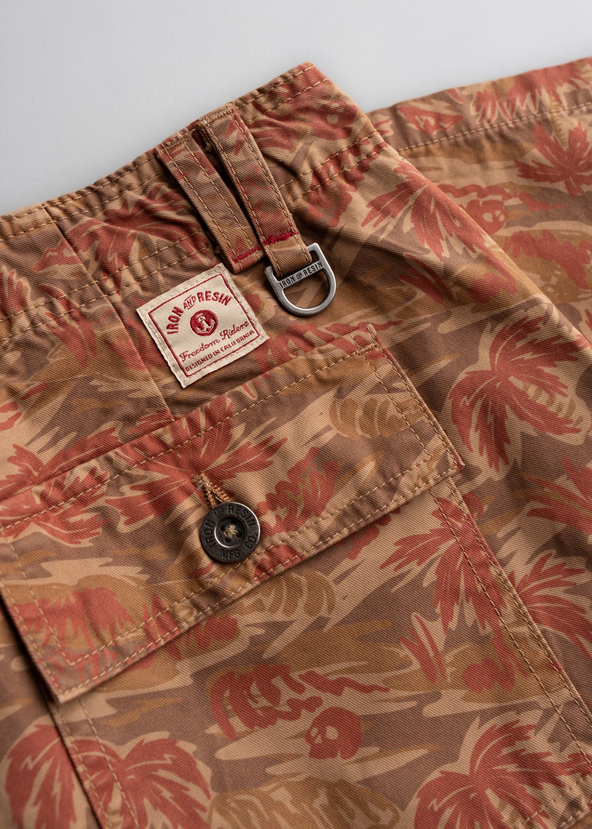 Close-up of brown and red floral shorts with a buttoned pocket, D-ring, and Iron and Resin label, showcasing detailed stitching.