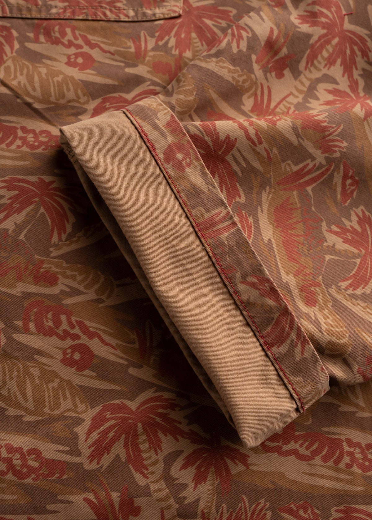 Close-up of a folded sleeve on a brown shirt with a red palm tree pattern, highlighting the detailed stitching and design.