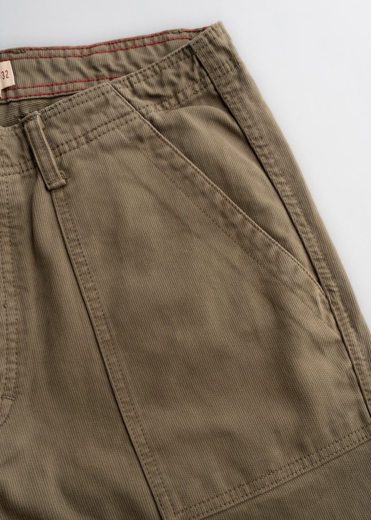 Close-up of khaki pants with visible stitching and a red-lined waistband, showcasing pocket detail and fabric texture.