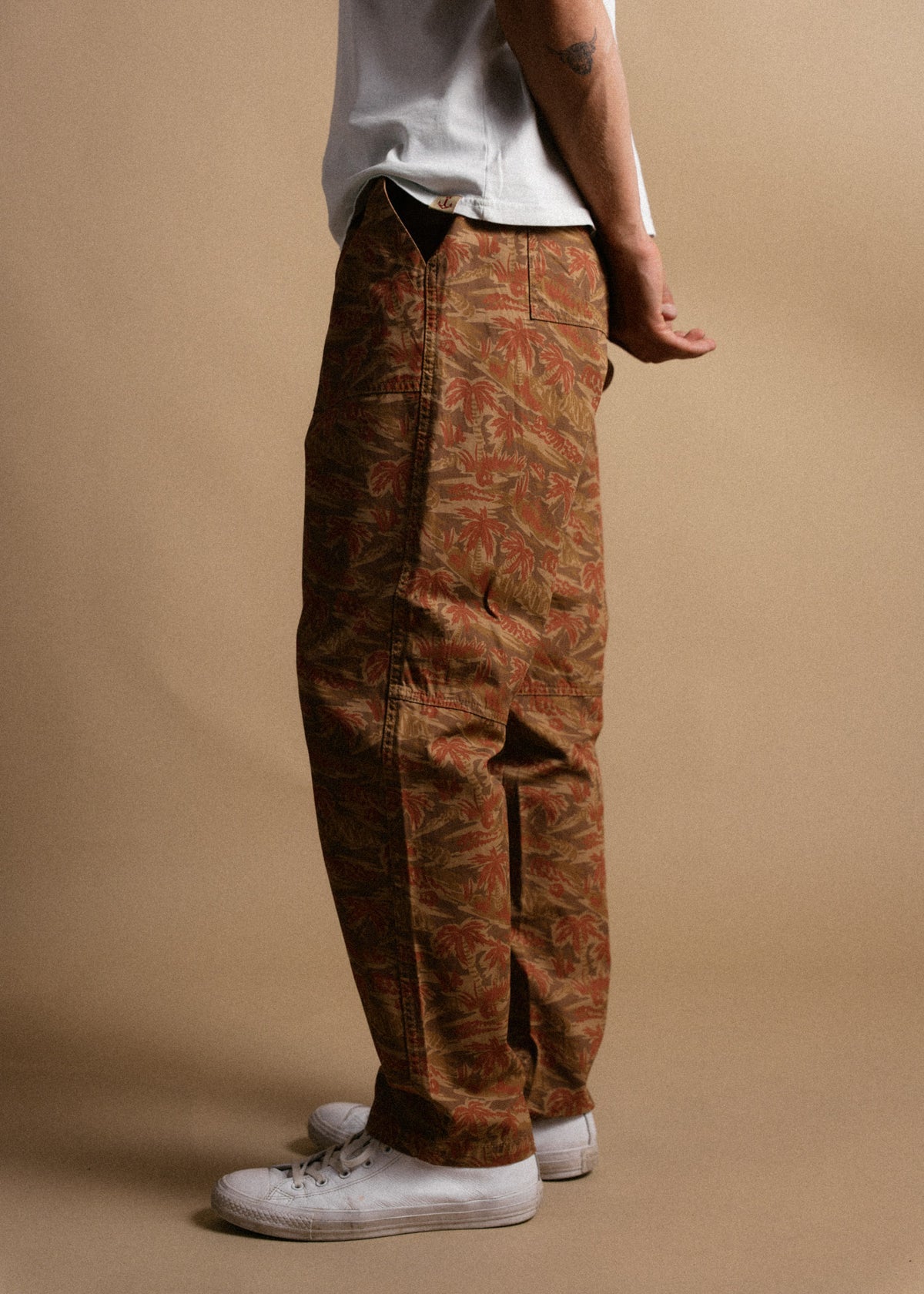 A person in floral cargo pants and white sneakers stands against a beige background, showcasing casual style.