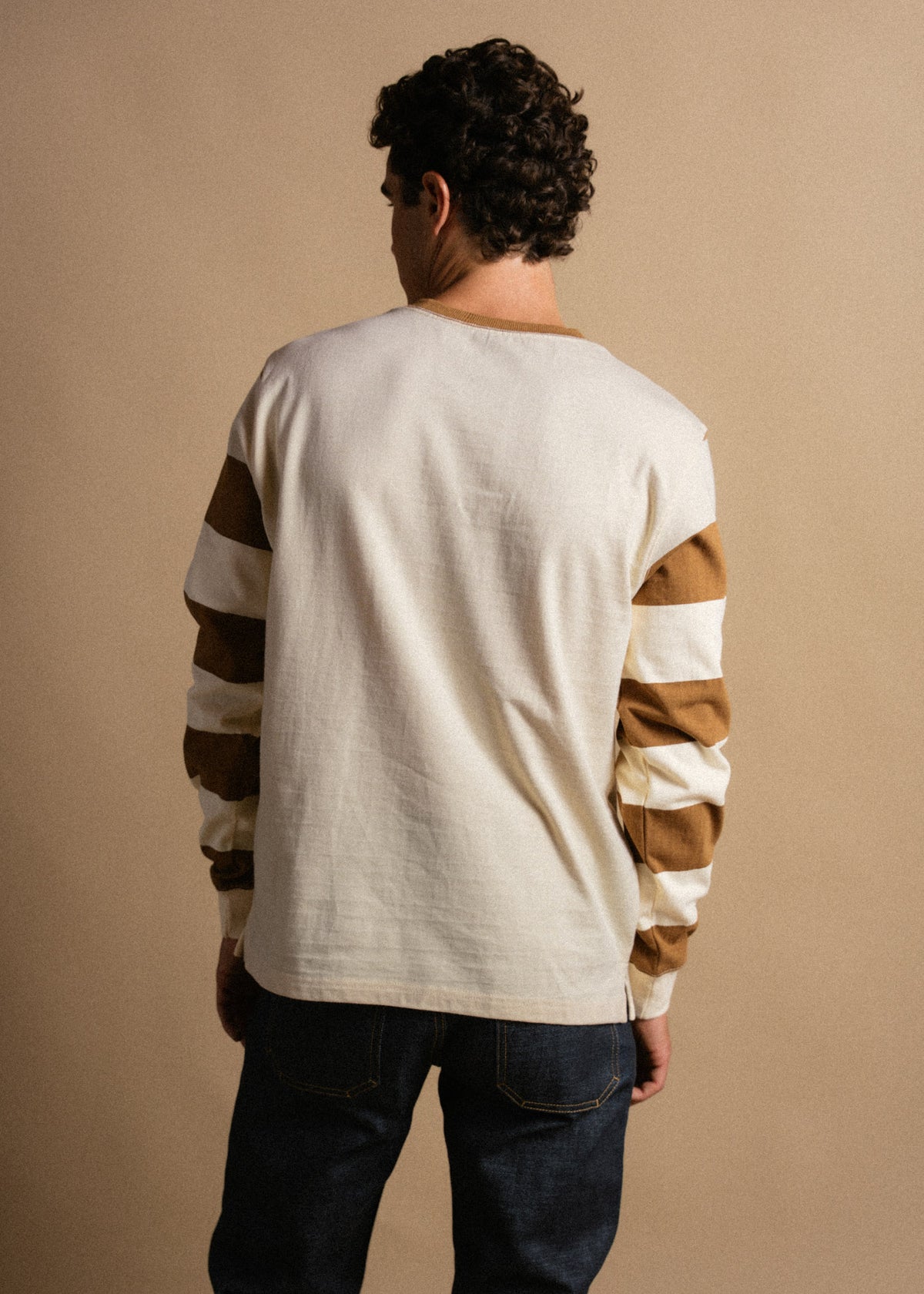 Man in a white shirt with brown striped sleeves, facing away, against a beige background. Casual and stylish look.