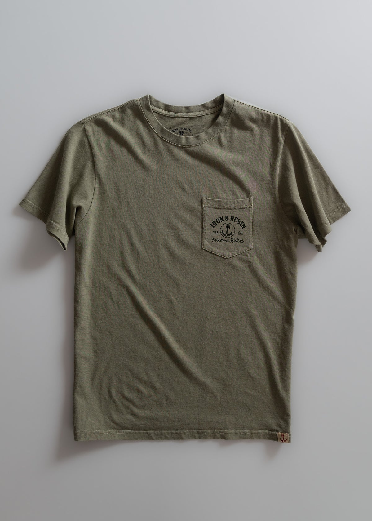 Olive green T-shirt with a chest pocket featuring "Iron & Resin" logo and "Freedom Riders" text, laid flat on a light surface.