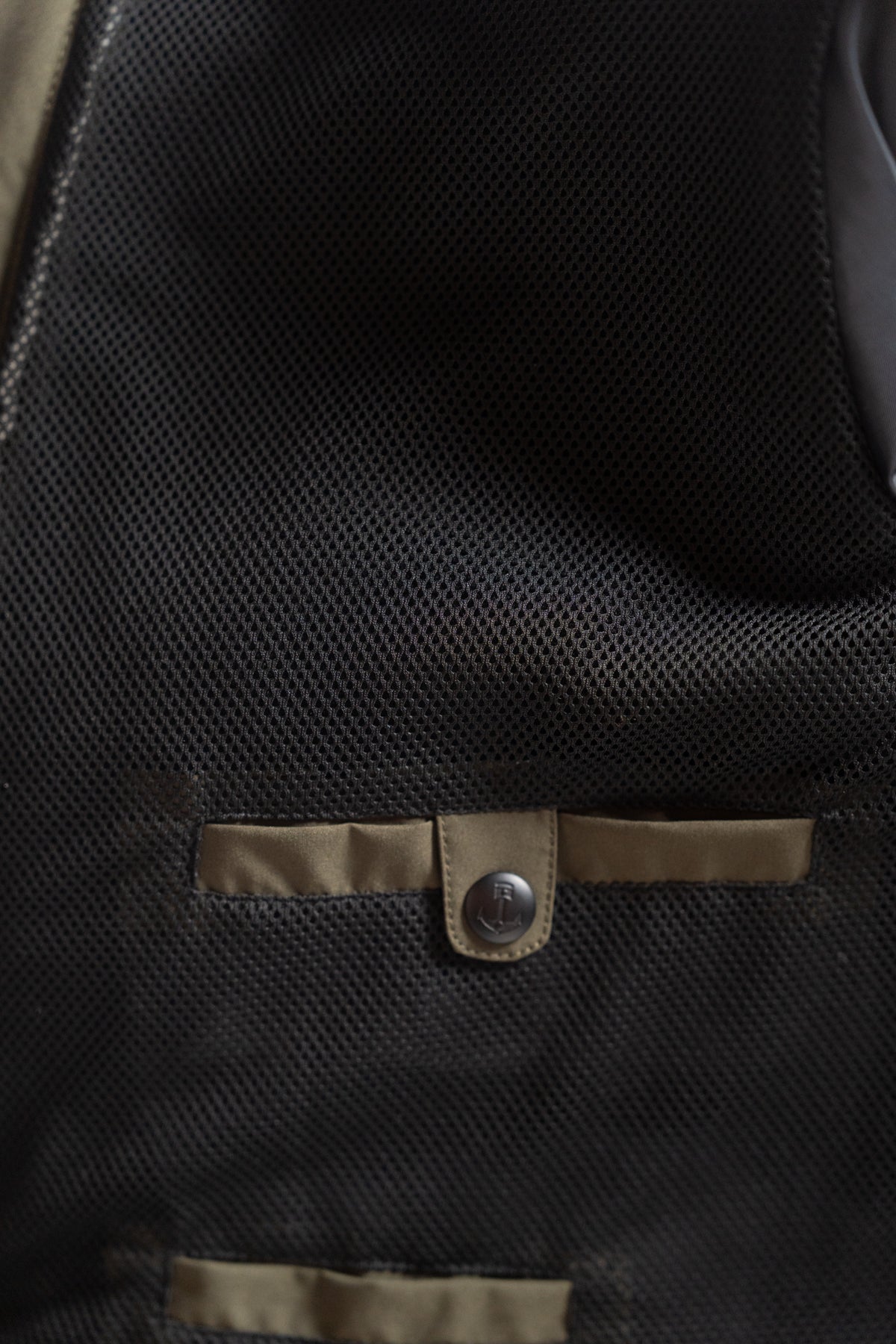 Close-up of a black mesh fabric with beige trim and a button, showcasing texture and detail in a garment or accessory.