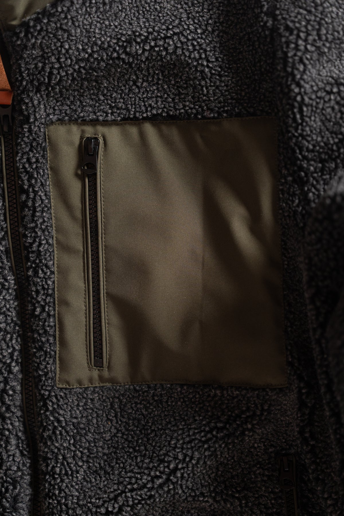Close-up of a dark fleece jacket with a green zippered pocket, showcasing texture and design details in soft lighting.