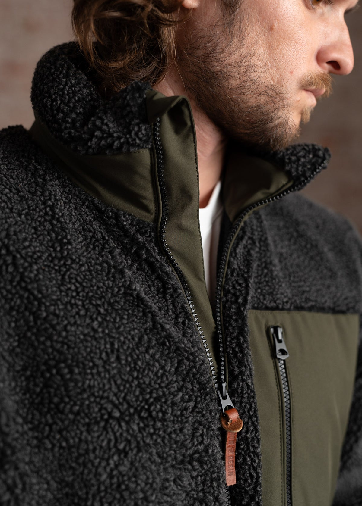 Man in a cozy black fleece jacket with green accents, close-up on zipper and collar, showcasing texture and design details.