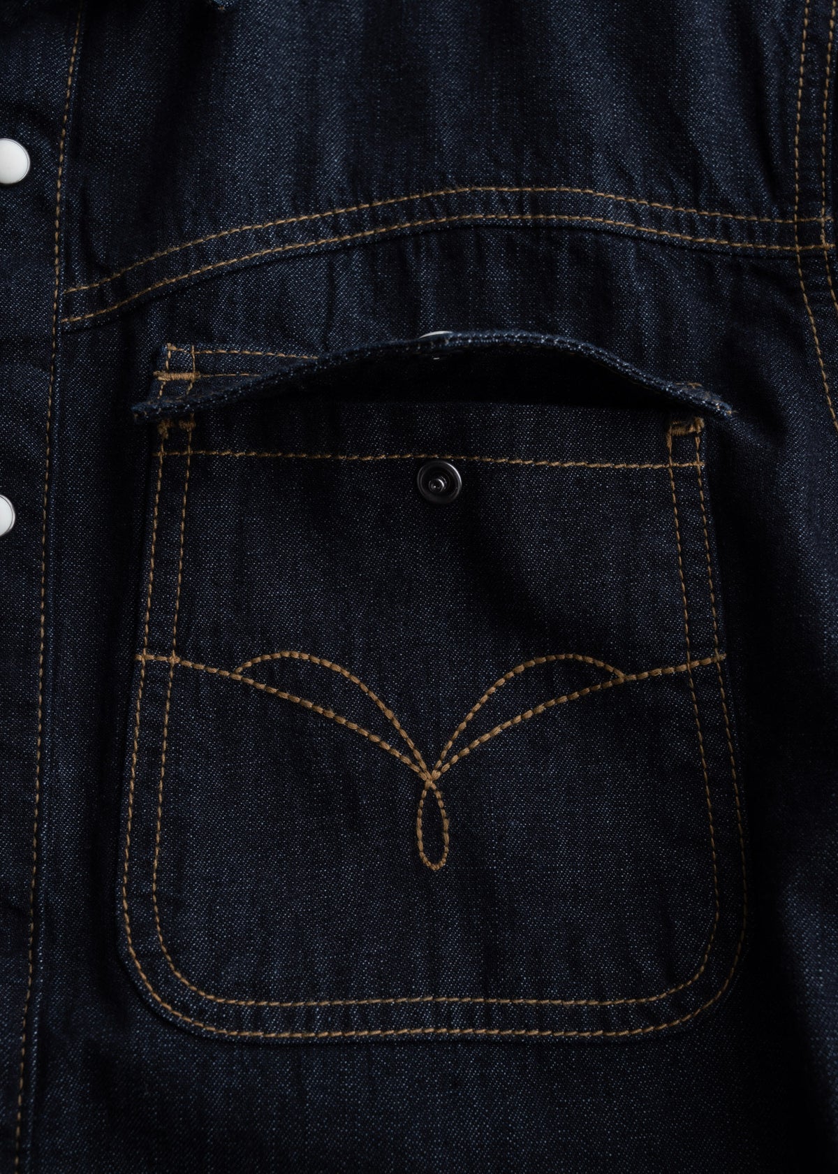 Close-up of a denim jacket pocket with yellow stitching and a button, showcasing detailed craftsmanship and classic design.