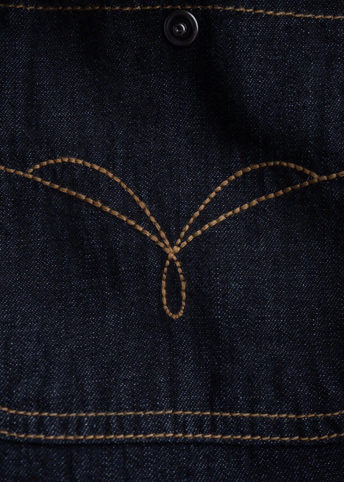 Close-up of dark blue denim fabric with intricate brown stitching and a black button, showcasing detailed craftsmanship.