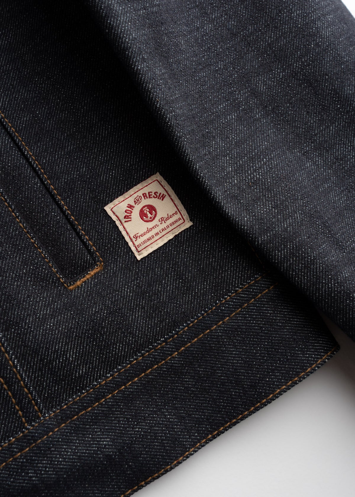 Close-up of a dark denim jacket with a visible "Iron and Resin" label, highlighting its textured fabric and stitching details.