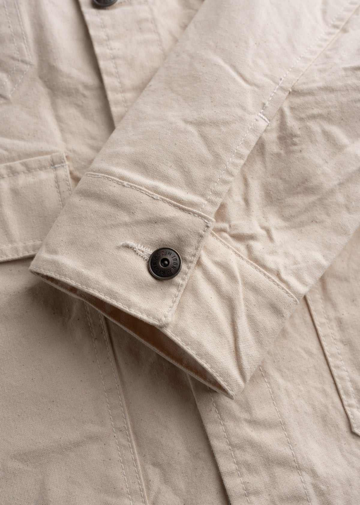Close-up of a beige jacket sleeve with a black button, highlighting its texture and stitching detail.