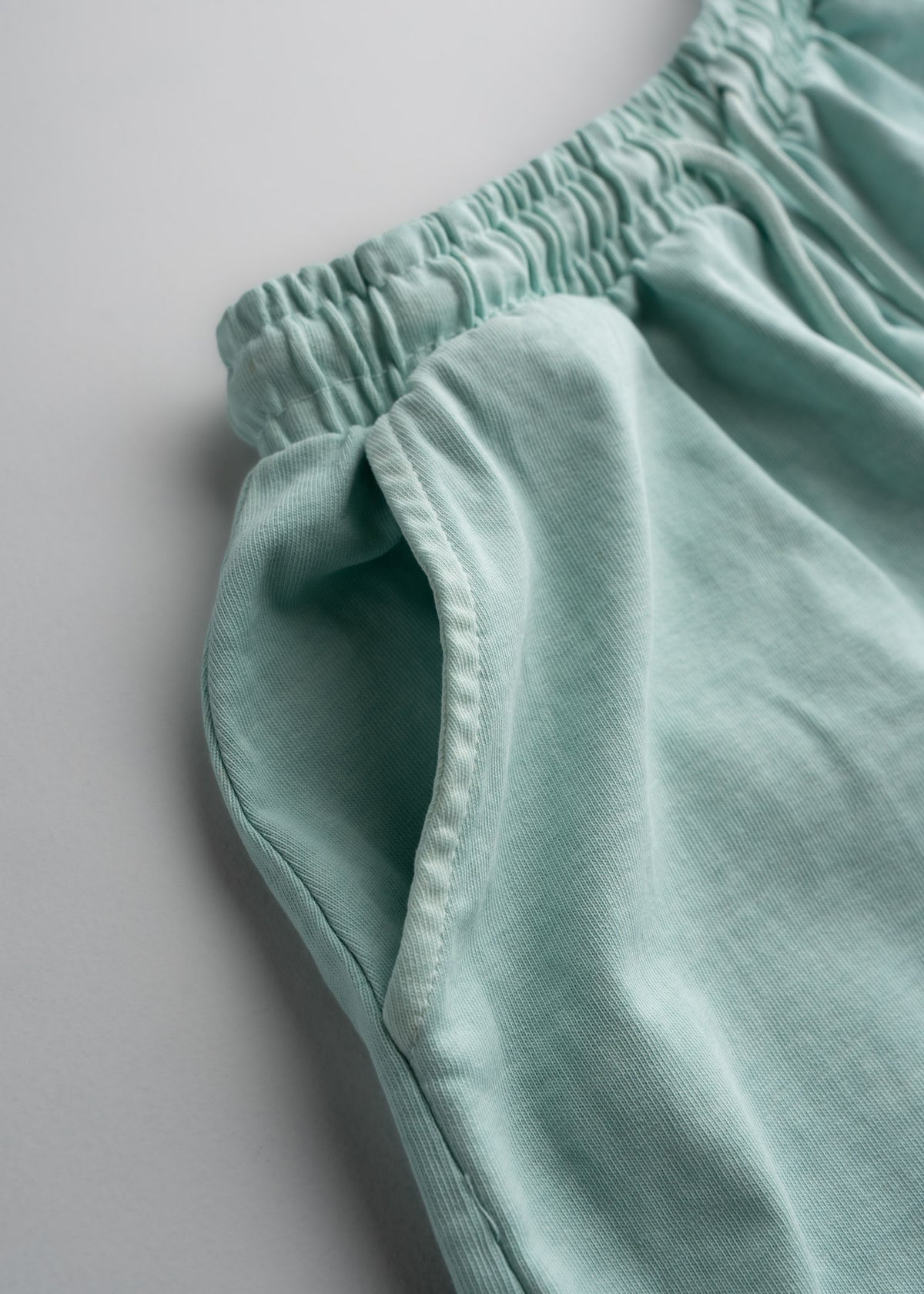 Close-up of light green shorts with an elastic waistband and side pocket, showcasing soft fabric texture and casual style.