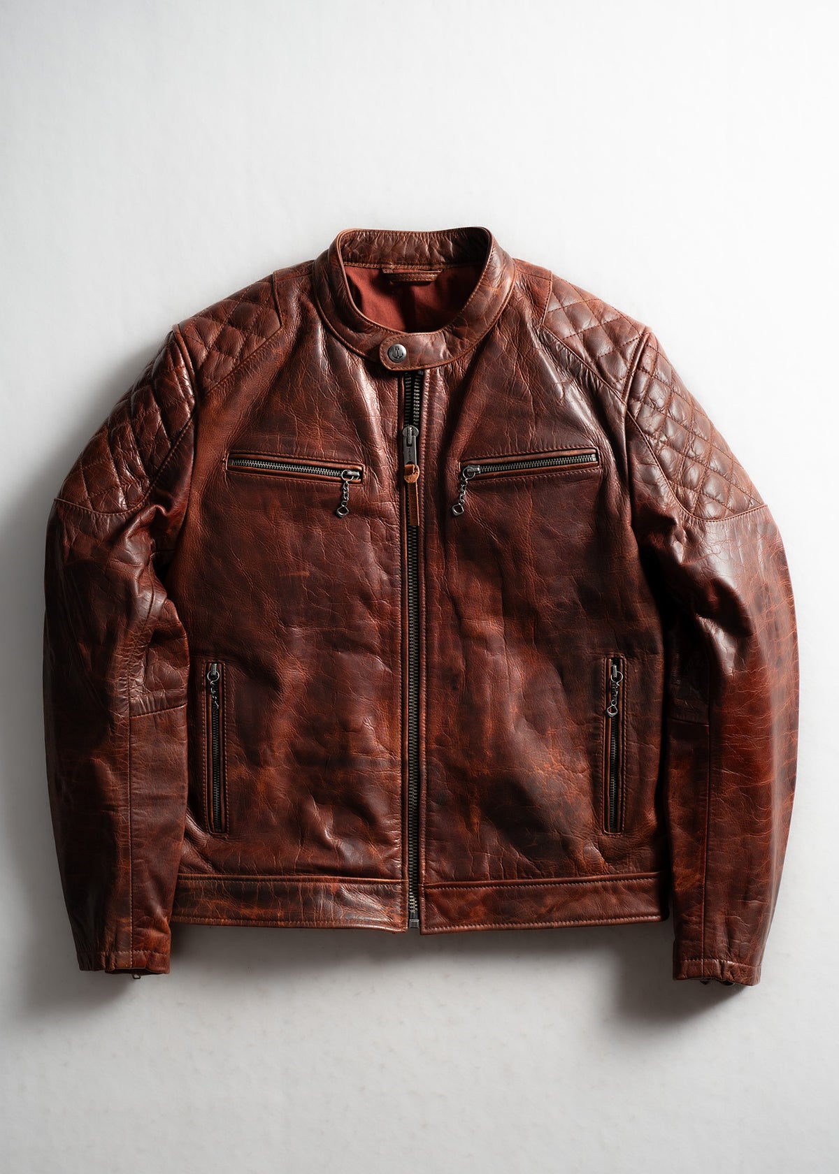 Brown leather jacket with quilted shoulders, front zipper, and pockets, laid flat on a light background.