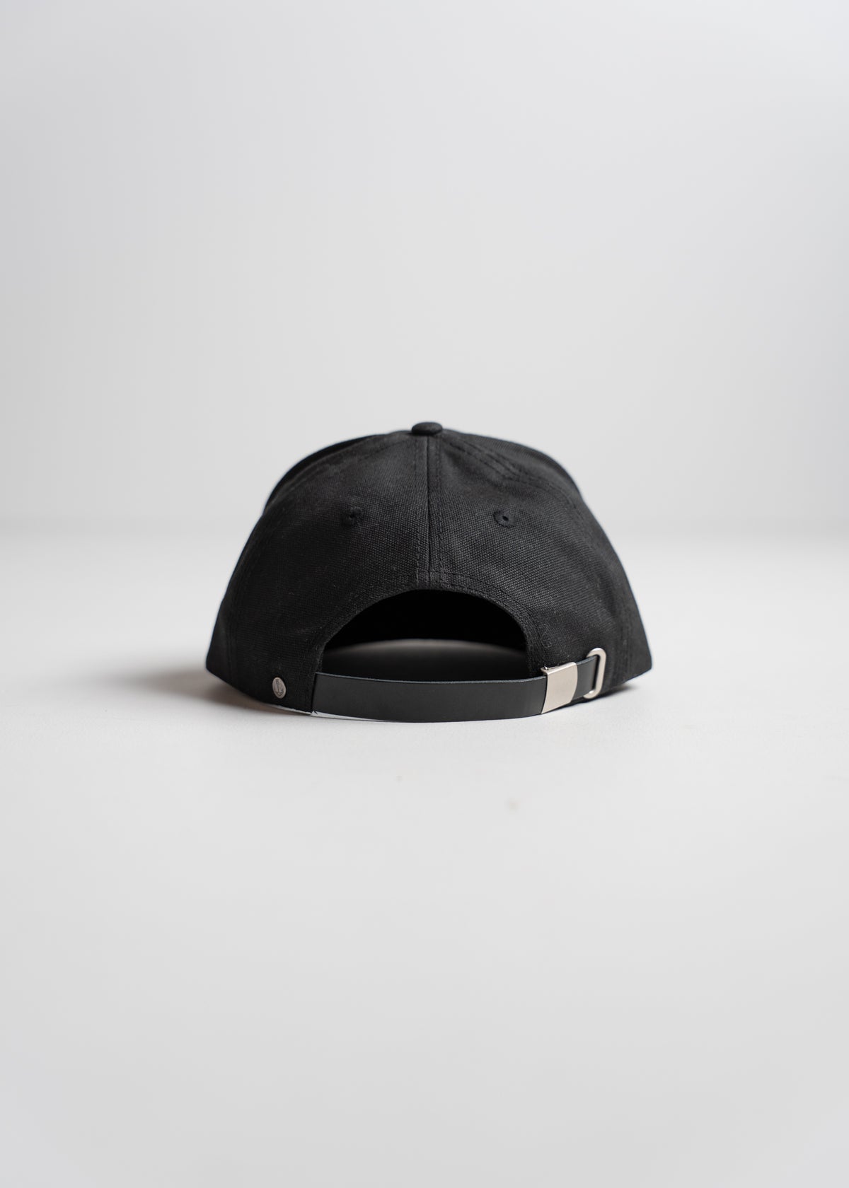 A black baseball cap viewed from the back, showcasing an adjustable strap and buckle, set against a plain white background.