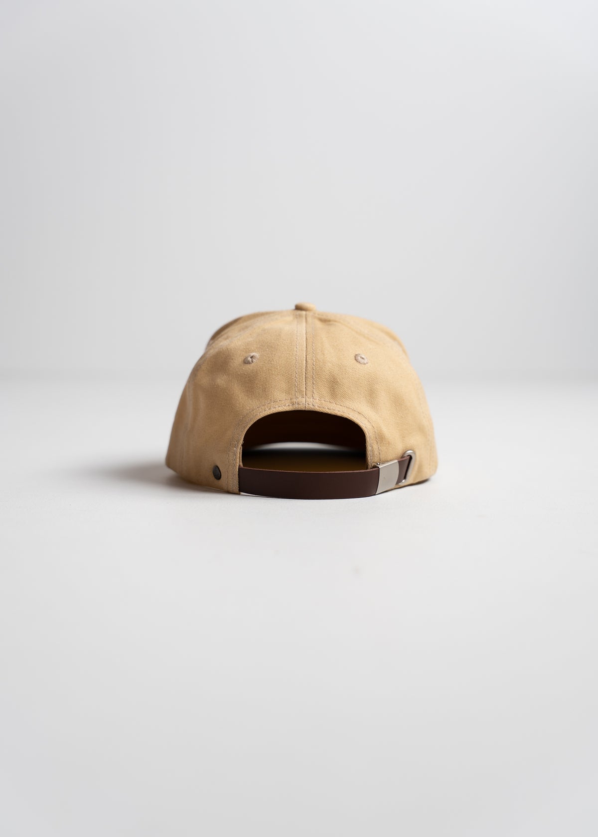 Tan baseball cap with a brown adjustable strap, viewed from the back on a plain white background.