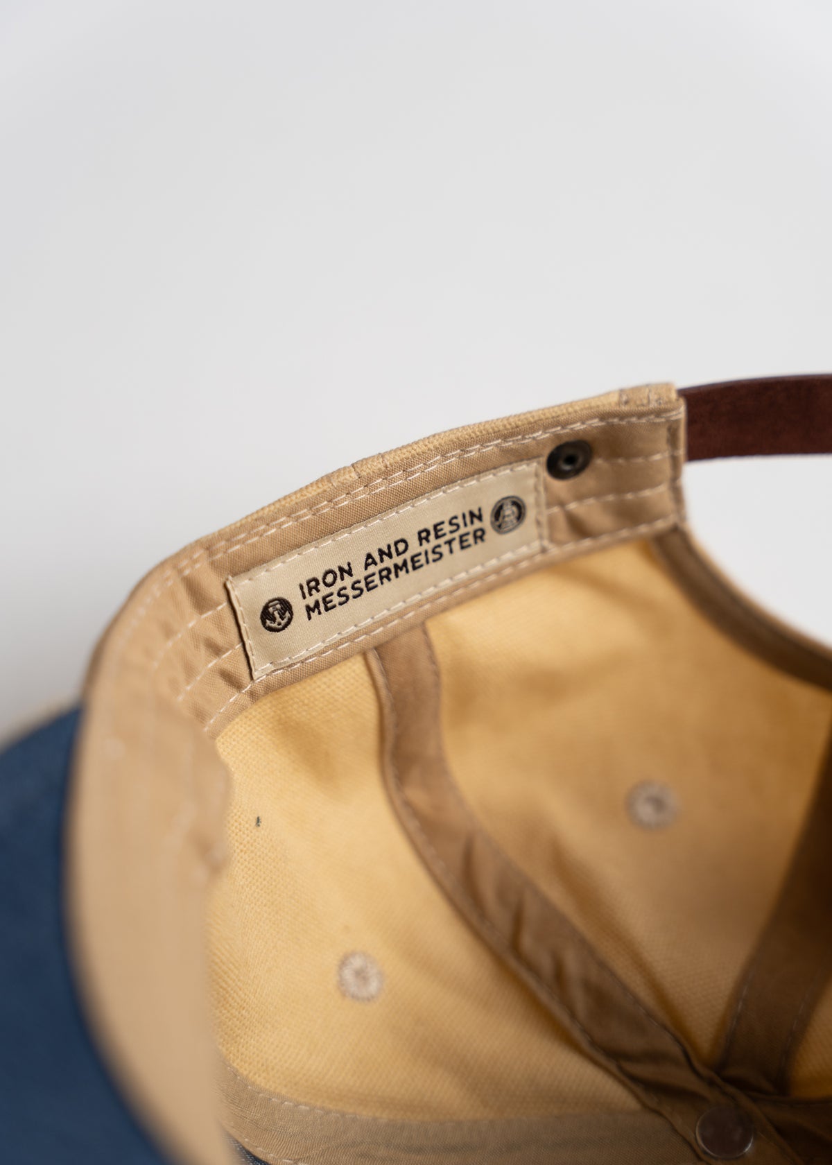 Inside view of a tan cap showing a label with "Iron and Resin Messermeister" text, highlighting the brand collaboration.