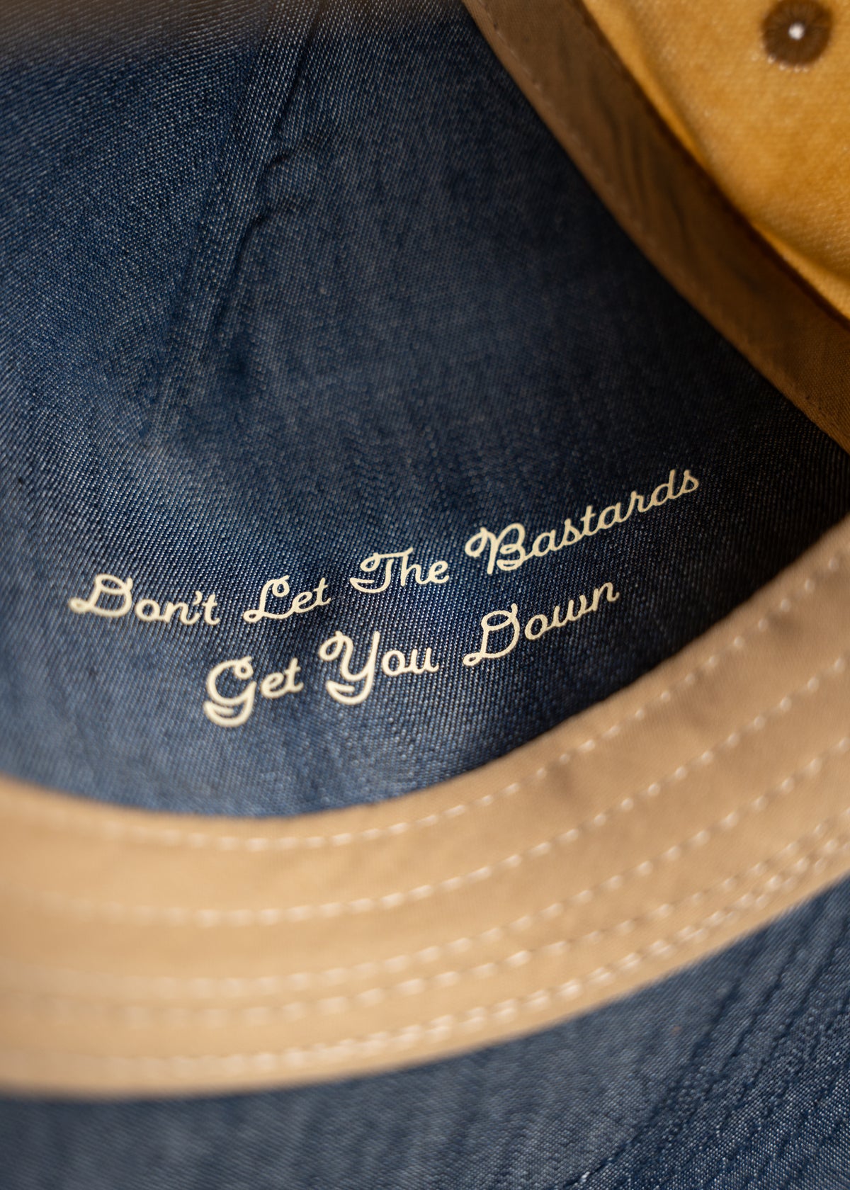 Close-up of a hat with the phrase "Don't Let The Bastards Get You Down" embroidered inside, offering an empowering message.