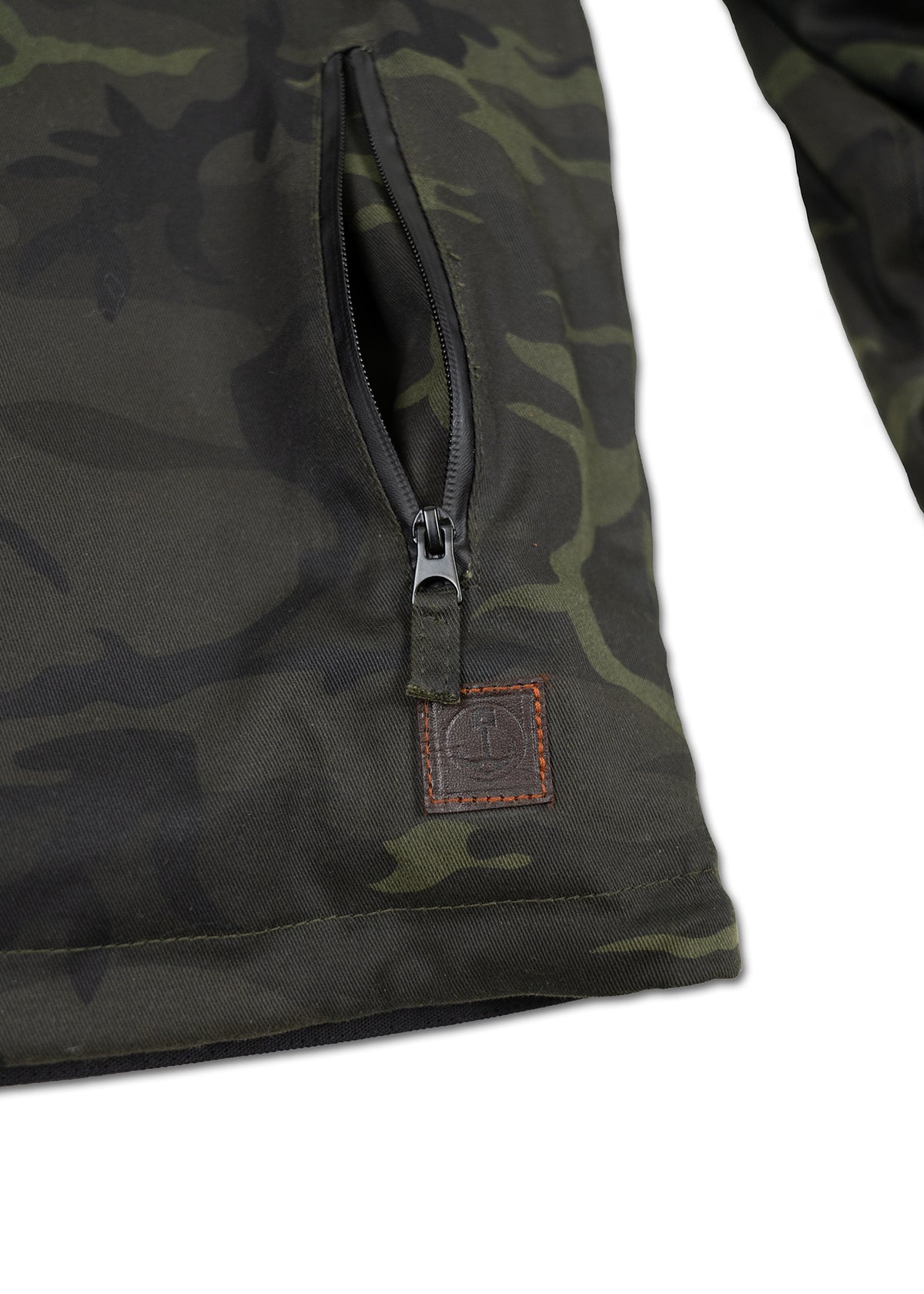 Camouflage jacket close-up showing a zippered pocket and a small leather patch with stitching detail on the lower side.