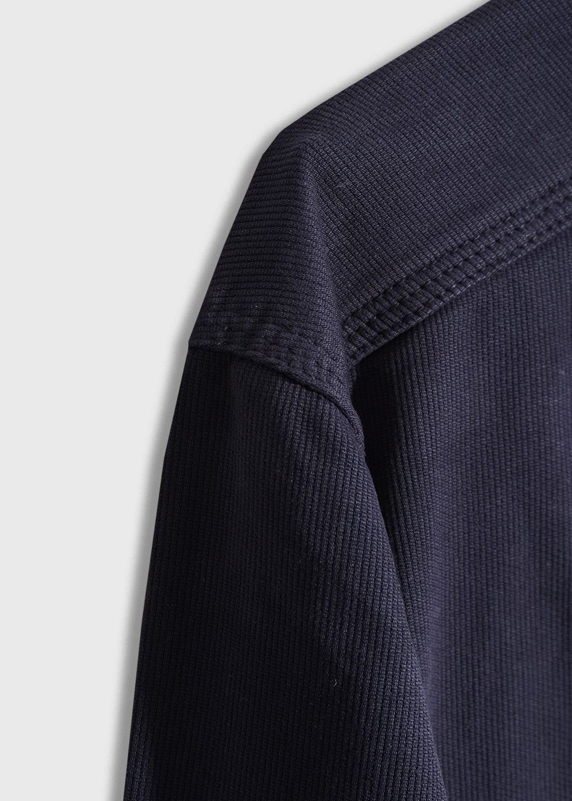 Close-up of a navy blue textured fabric on a garment, showing detailed stitching and ribbed pattern against a light gray background.