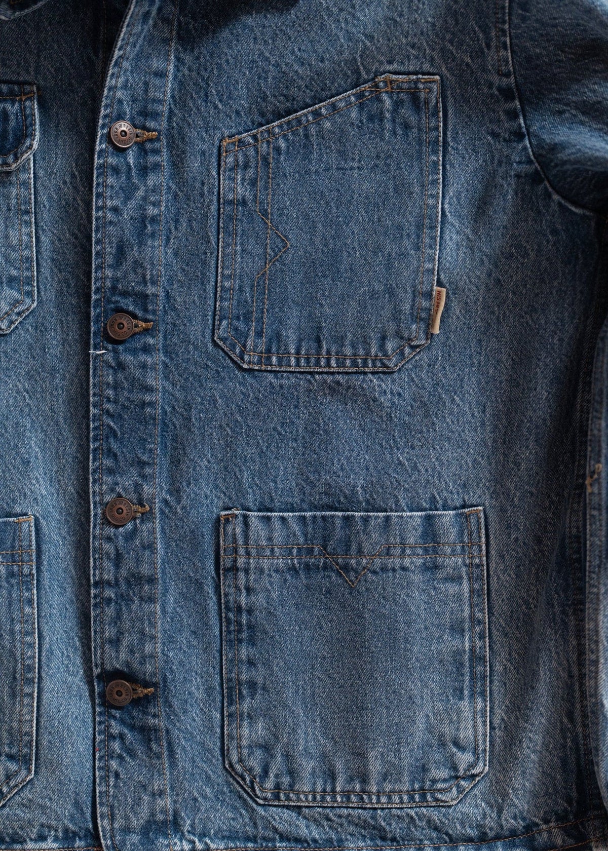 Close-up of a blue denim jacket with visible stitching, featuring two front pockets and button details.