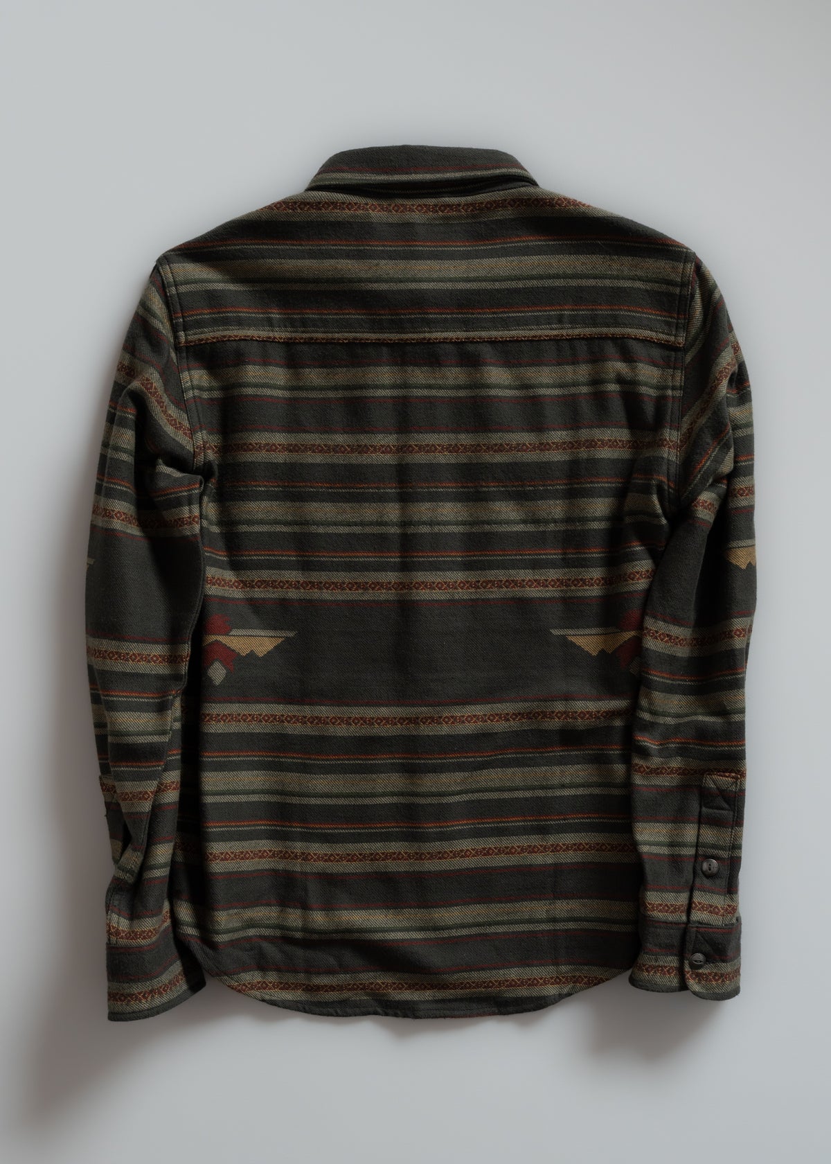 Back view of a long-sleeve shirt with green, brown, and red horizontal stripes and geometric patterns on a plain background.