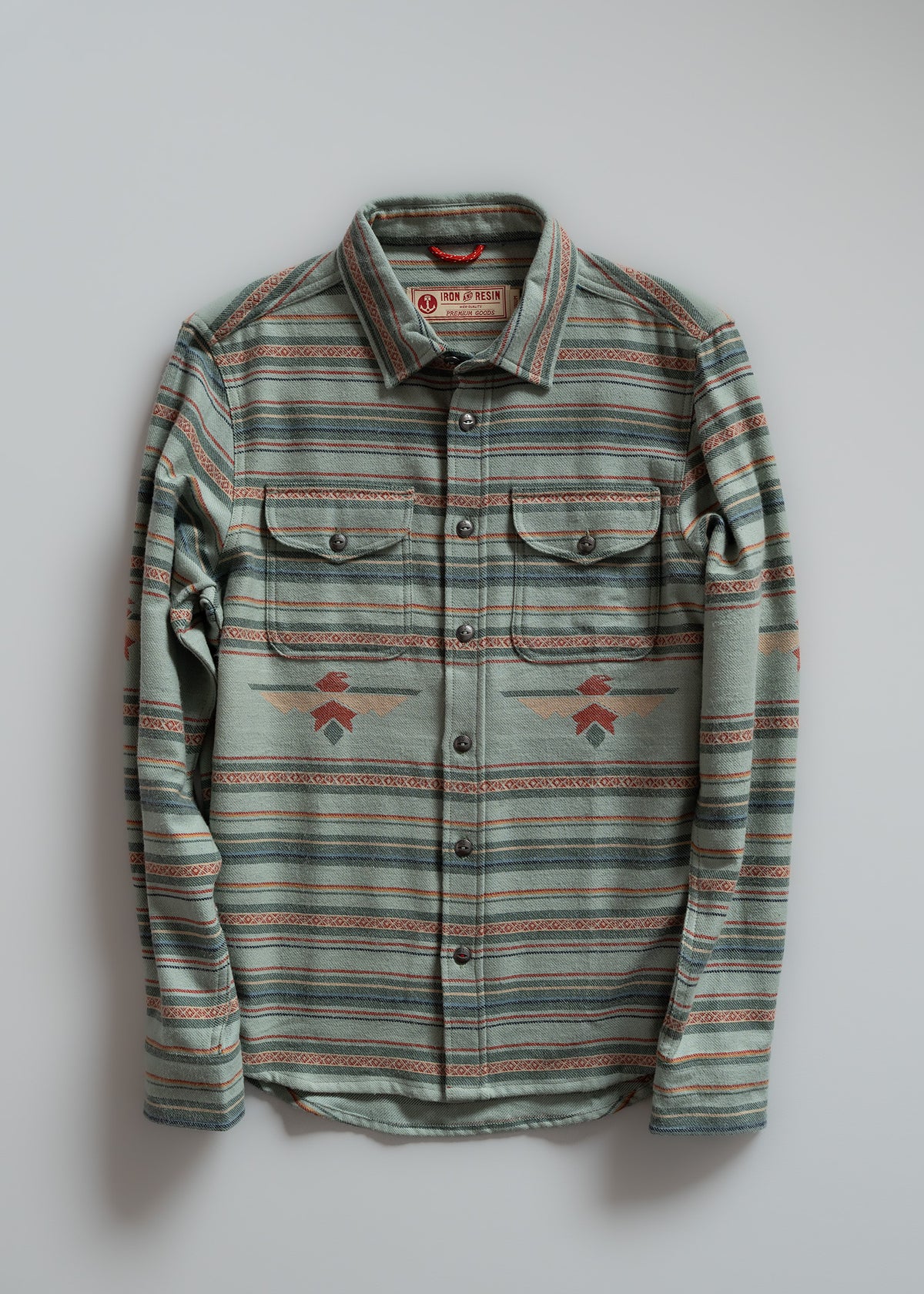 Striped green flannel shirt with buttoned pockets, featuring geometric patterns, displayed on a light gray background.