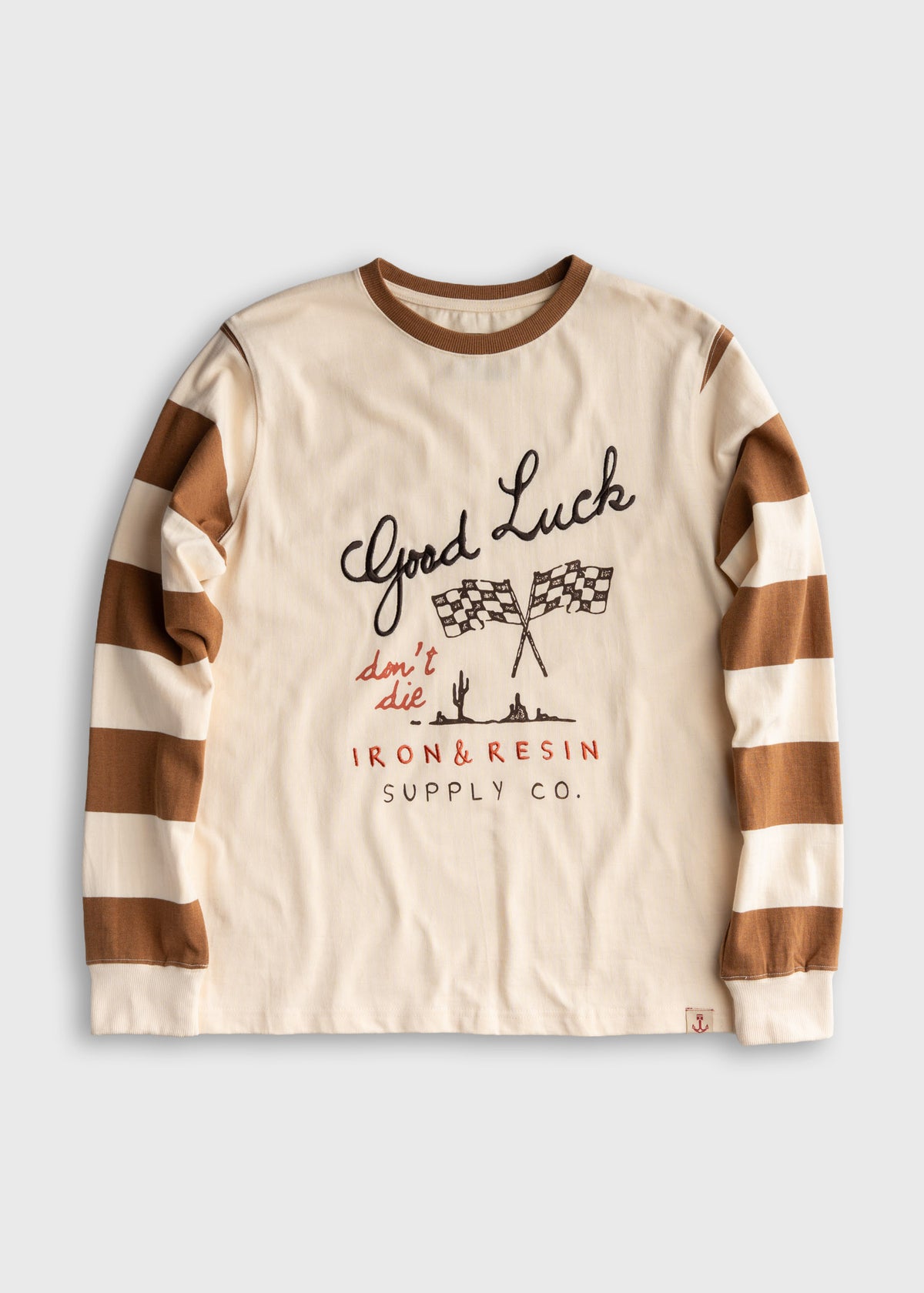 Cream shirt with brown striped sleeves, "Good Luck" text, checkered flags, and "Iron & Resin Supply Co." printed on the front.