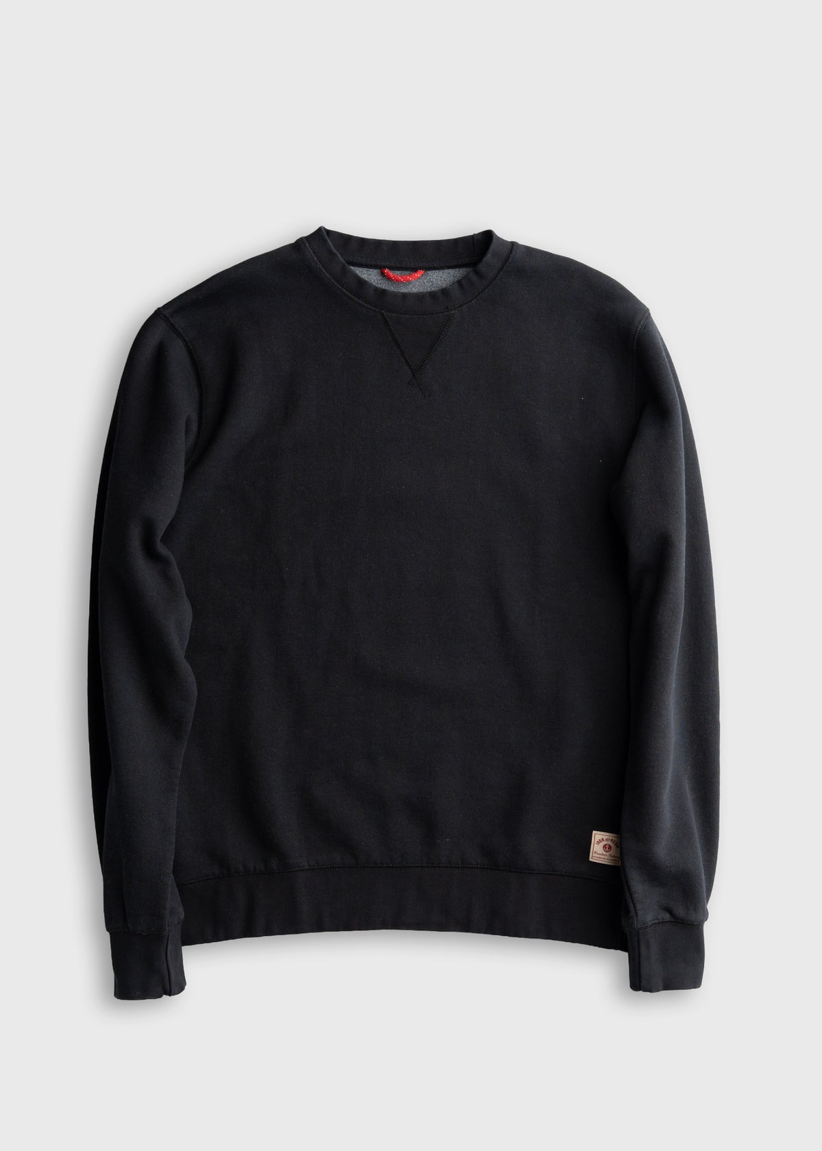Black crewneck sweatshirt with long sleeves and a small logo patch on the hem, displayed on a plain white background.