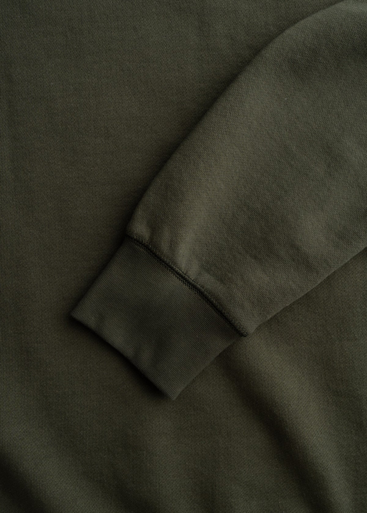 Close-up of a dark green sweatshirt sleeve on a matching fabric background, highlighting the texture and stitching detail.
