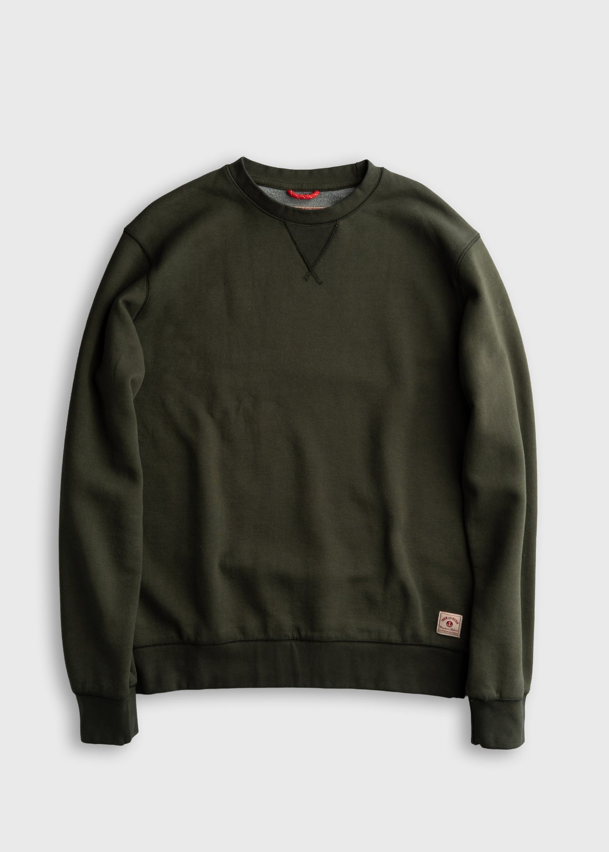 Dark green crewneck sweatshirt with ribbed cuffs and hem, featuring a small logo patch on the lower left side.