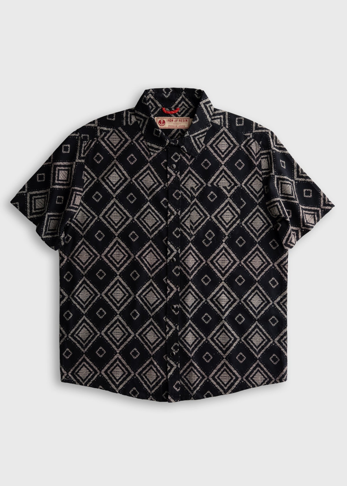 Short-sleeve shirt with geometric diamond pattern on black fabric, featuring a collar and buttons, labeled "Iron & Resin."