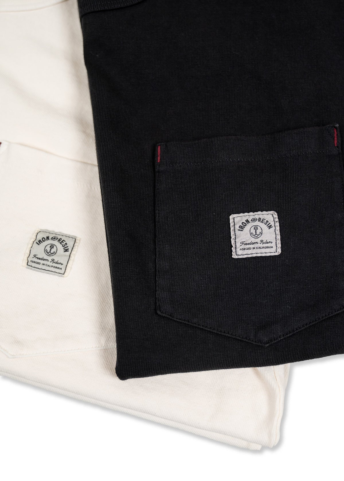 Black and white shirts with front pockets, featuring Iron and Resin labels, are neatly folded, showcasing minimalist style.
